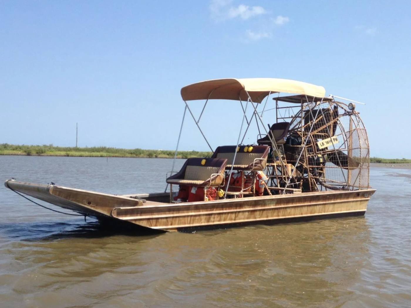 Side view of the tan canopy airboat, showing its benches and propeller cage