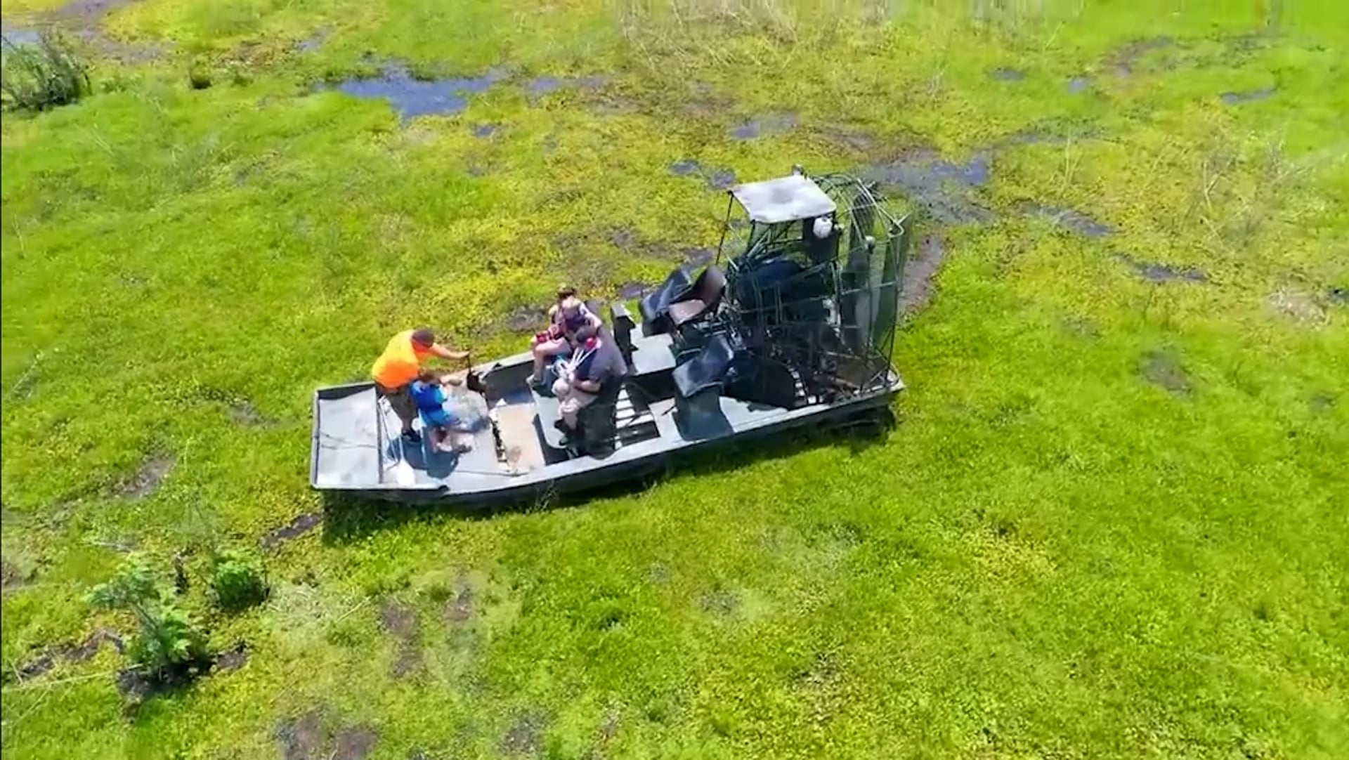 A captain in an orange shirt with two young riders on an airboat, seen from above